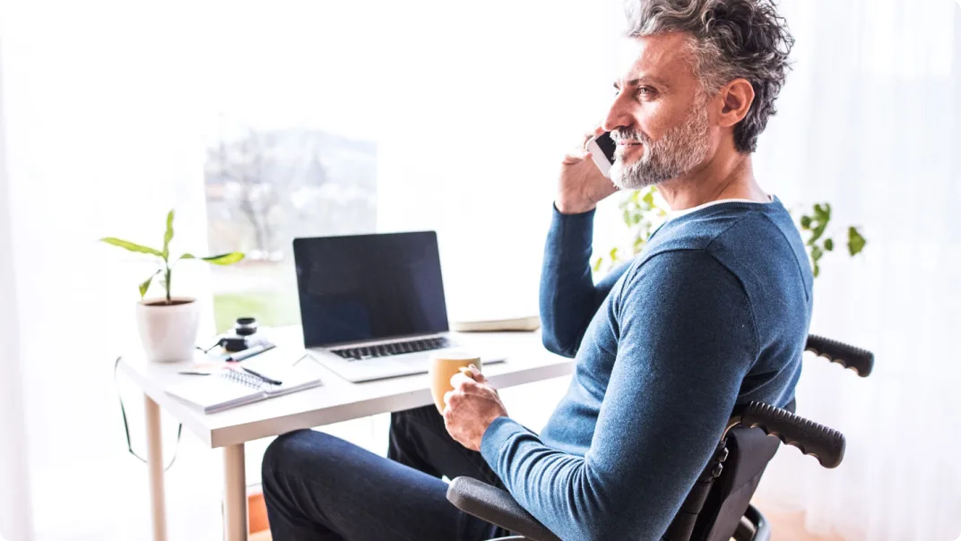 A man sitting at his desk in a wheelchair speaks on his smartphone