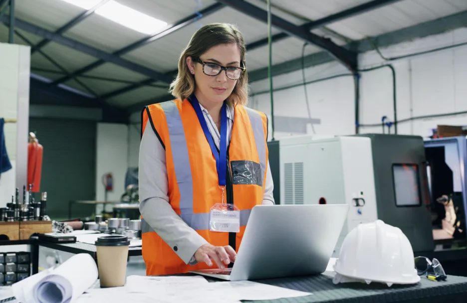 Connected worker wearing orange safety vest and safety goggles while working on a laptop