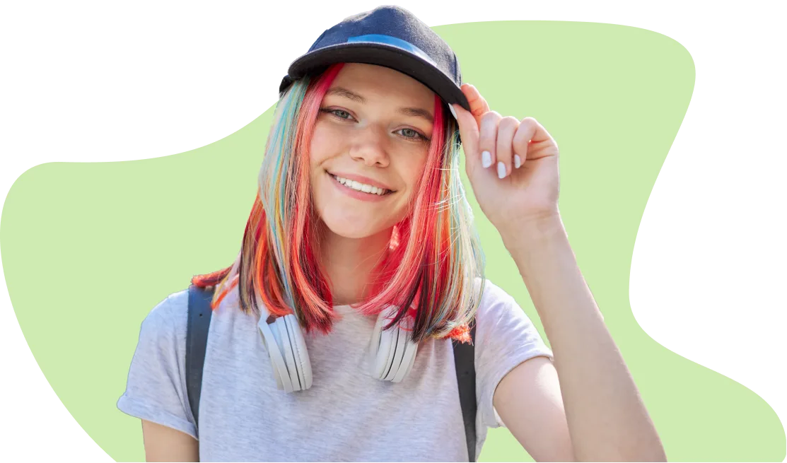 Une adolescente aux cheveux colorés portant une casquette et souriant à l’appareil photo.