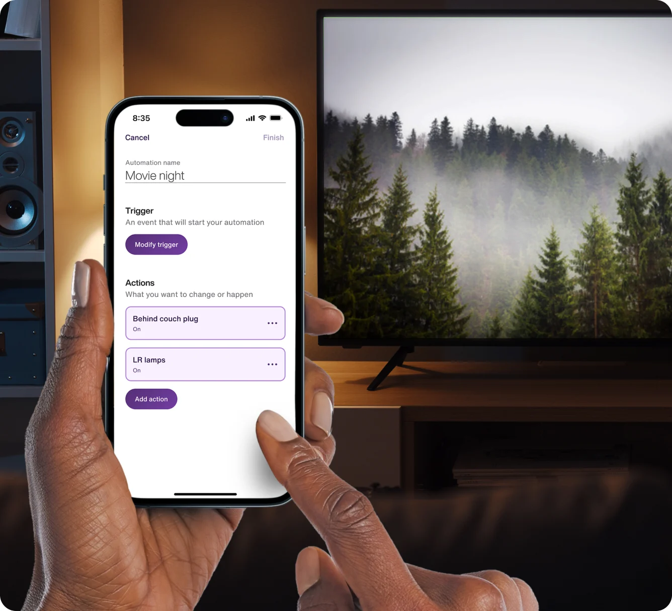 A hand holds the TELUS SmartHome+ app while getting ready to watch a movie at home. It is showing a customized Movie Night routine to dim the lights. 