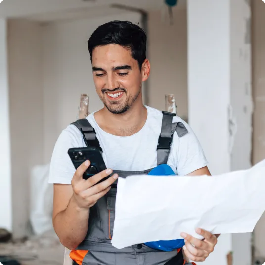 A man in a construction vest and hat looking at his tablet