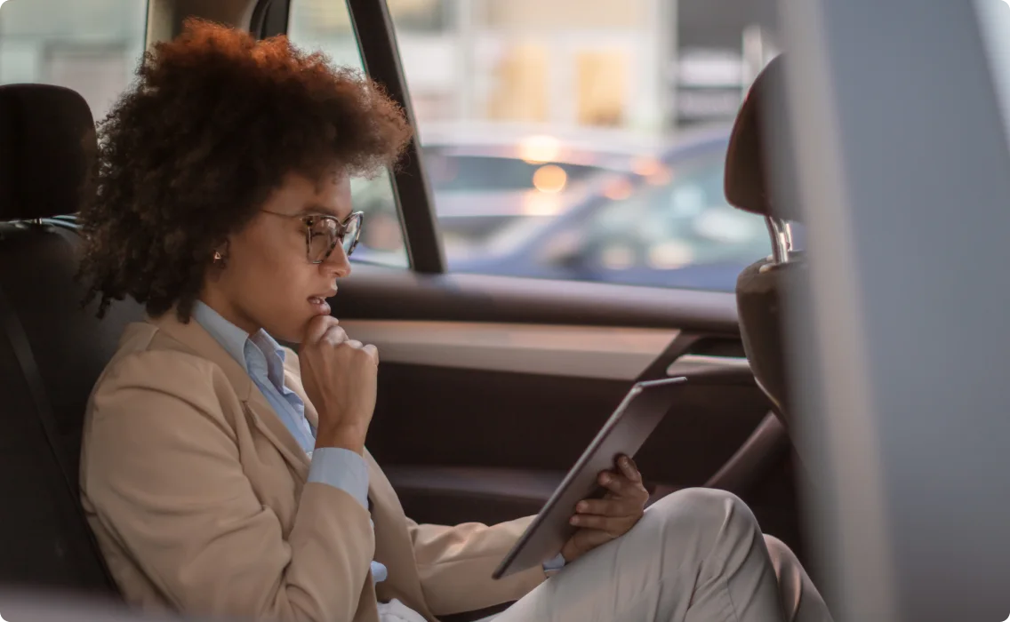 A women sitting in a car back seat looking at her tablet screen