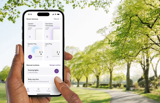 A hand holds the TELUS SmartHome+ app while out on a walk in the park showing the control of thermostats, smartplugs and routines.