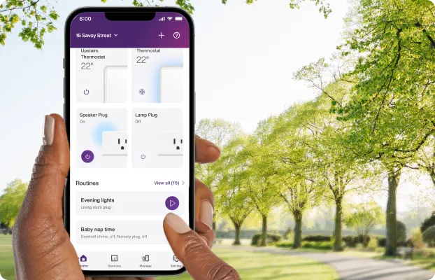 A hand holds the TELUS SmartHome+ app while out on a walk in the park showing the control of thermostats, smartplugs and routines.