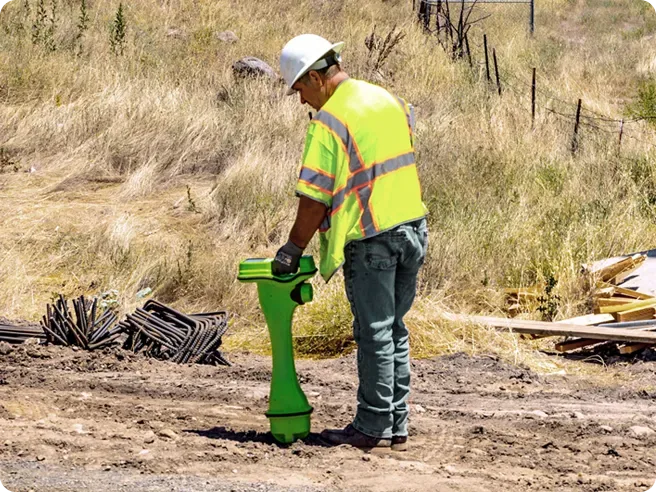 A Locate professional is in a field using a radio frequency detector to detect and identify utilities that are buried.