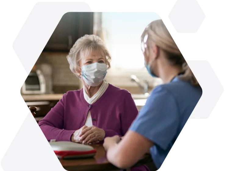 A lady wearing a face mask, speaking with a healthcare practitioner.