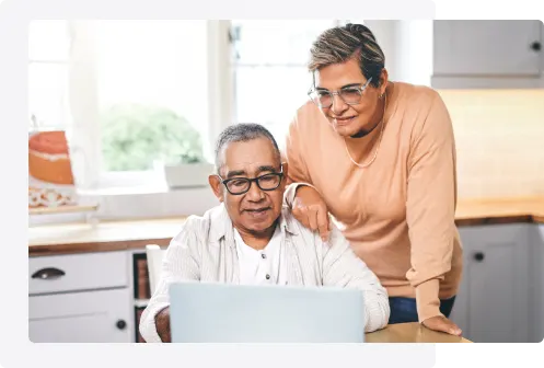 Un couple âgé est à l’ordinateur. La personne à gauche est assise et celle à droite s’appuie sur l’épaule de l’autre.