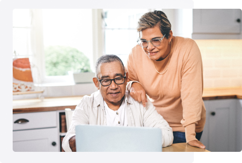 Un couple âgé est à l’ordinateur. La personne à gauche est assise et celle à droite s’appuie sur l’épaule de l’autre.