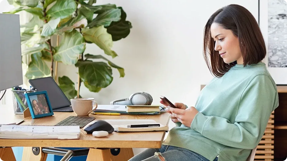 A woman is sitting in her home office accessing Pure Fibre internet through a smartphone.