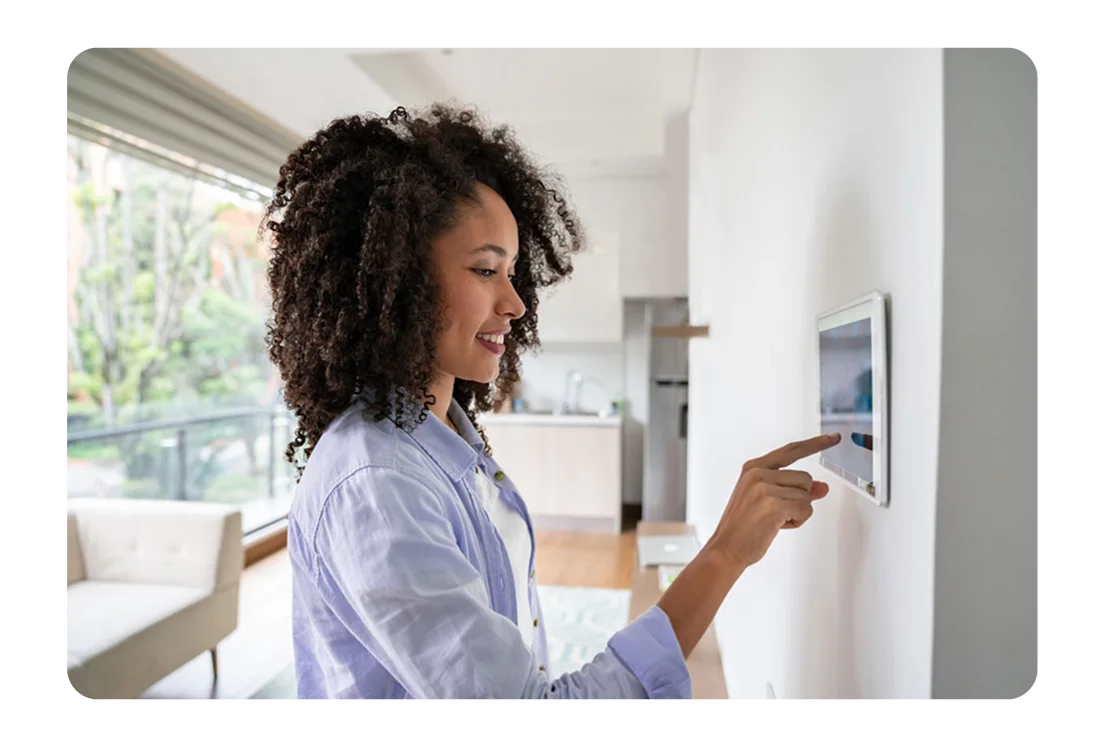 Smiling woman controls the SmartHome system on a wall mounted smart panel.