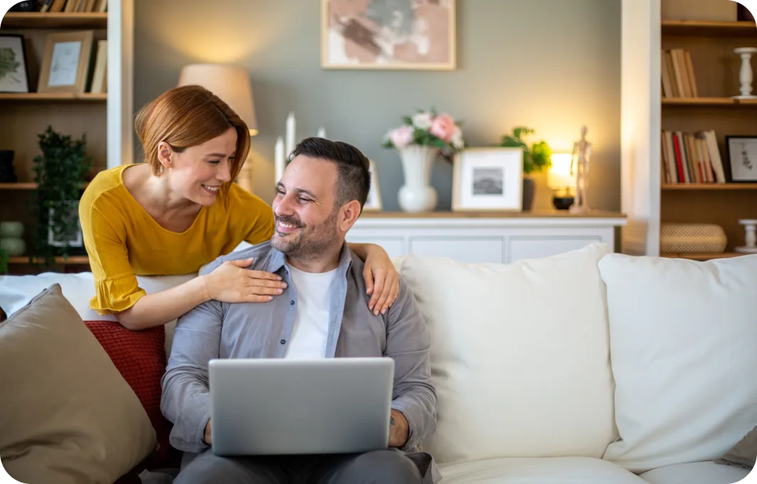 A couple sitting on a sofa and viewing their laptop.