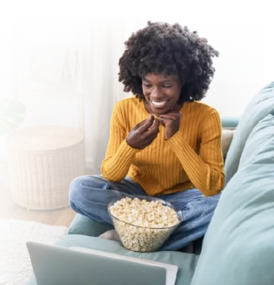 A woman sitting on the sofa with a bowl of popcorn, enjoying her favourite content on TELUS TV.