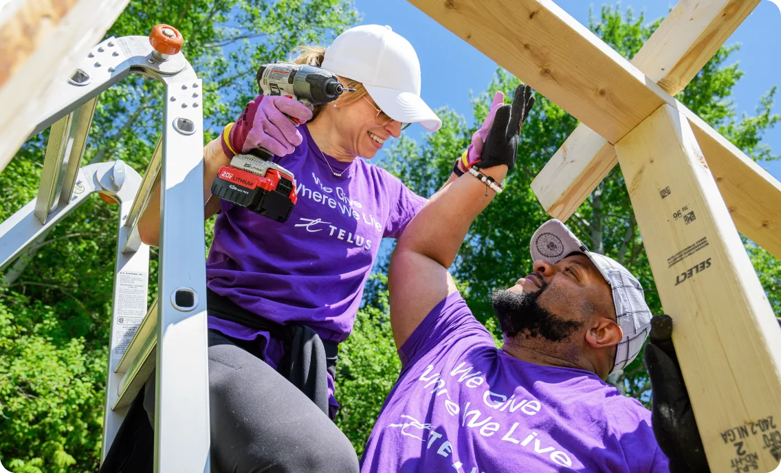 Two TELUS team members giving each other a high five while building a garden enclosure in a community garden.