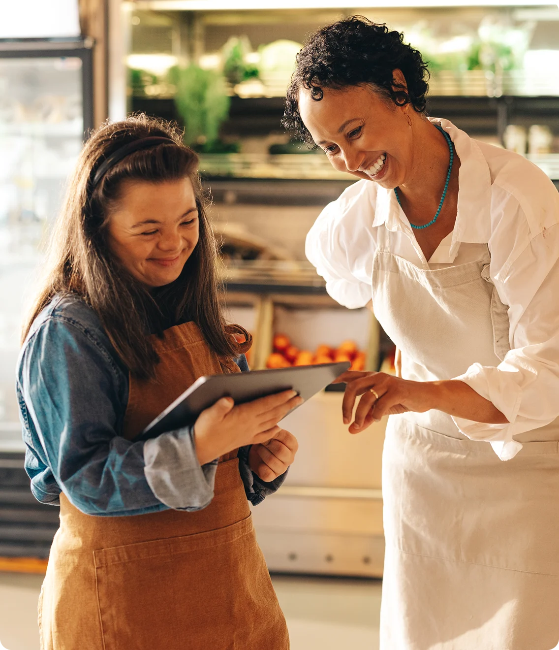 Shop manager trains an employee; both smiling while reviewing a tablet.