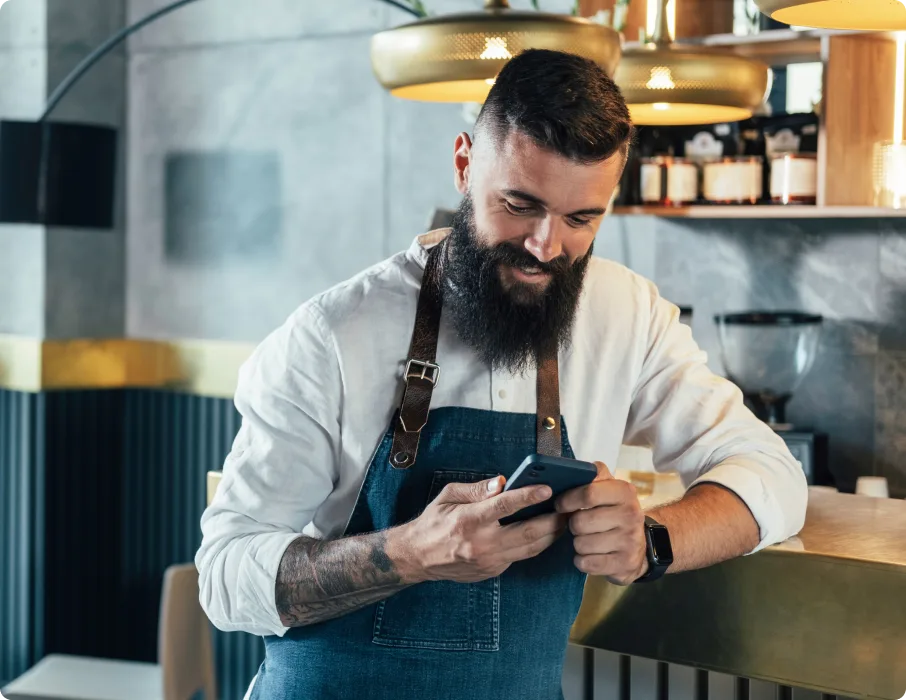 Restaurant staff member in apron using mobile phone in modern restaurant kitchen