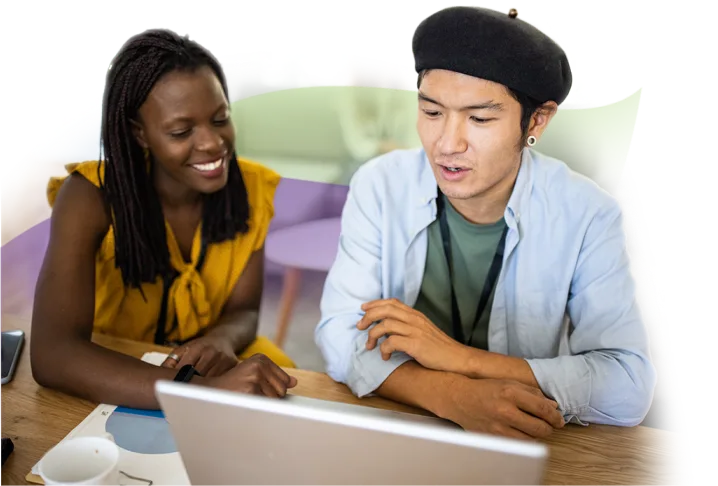 Two individuals sitting by a desk and viewing a laptop.