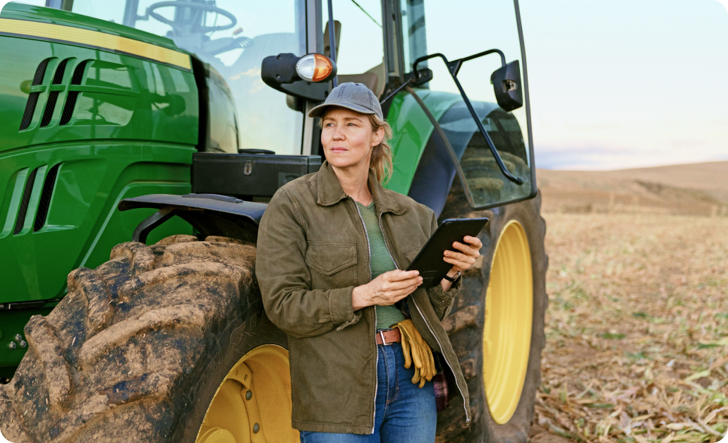 A farmer holding a tablet while standing beside her tractor in a field