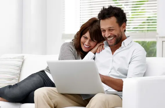 Un couple souriant sur un canapé regarde ensemble l'écran d'un ordinateur portable. 