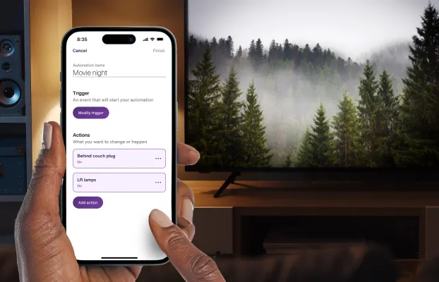 A hand holds the TELUS SmartHome+ app while getting ready to watch a movie at home. It is showing a customized Movie Night routine to dim the lights. 