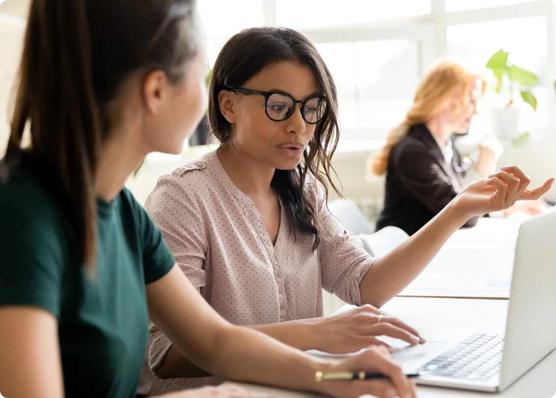 Two colleagues collaborating on laptop at office desk.