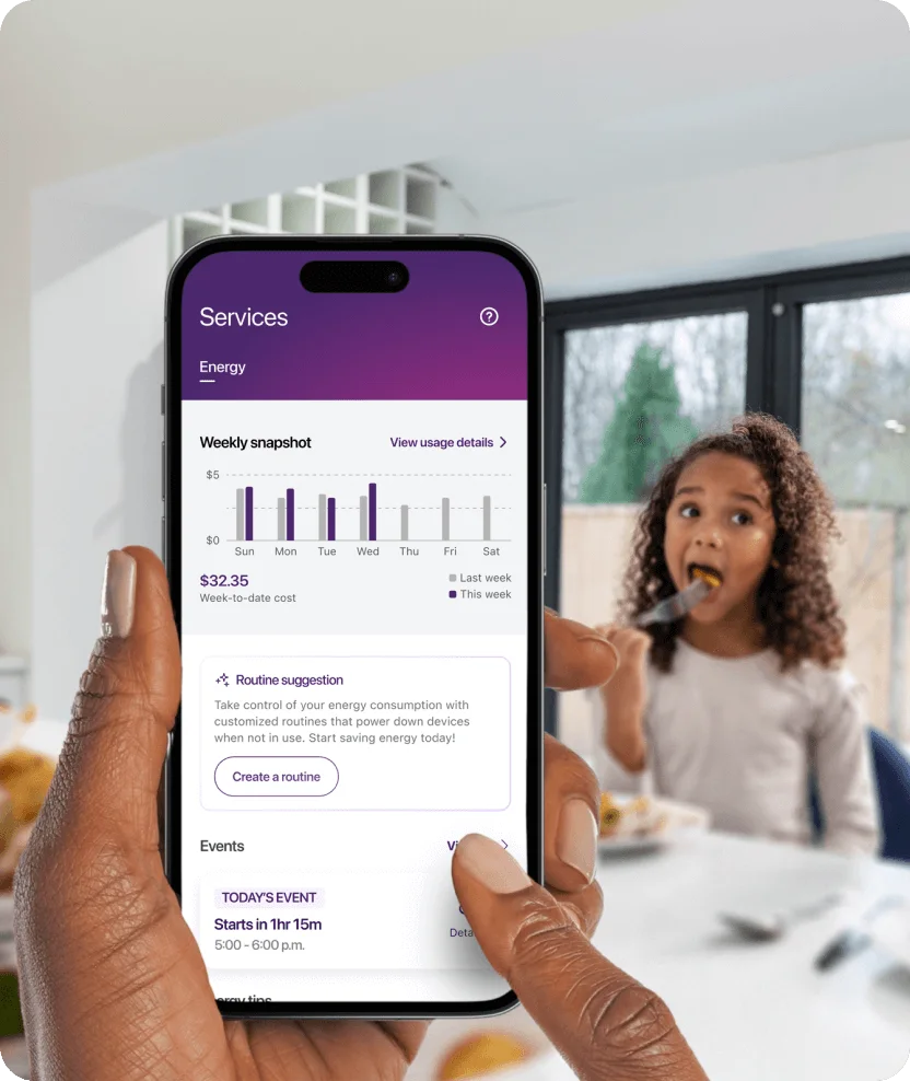 Hand holding smartphone showing energy consumption charts with family in background