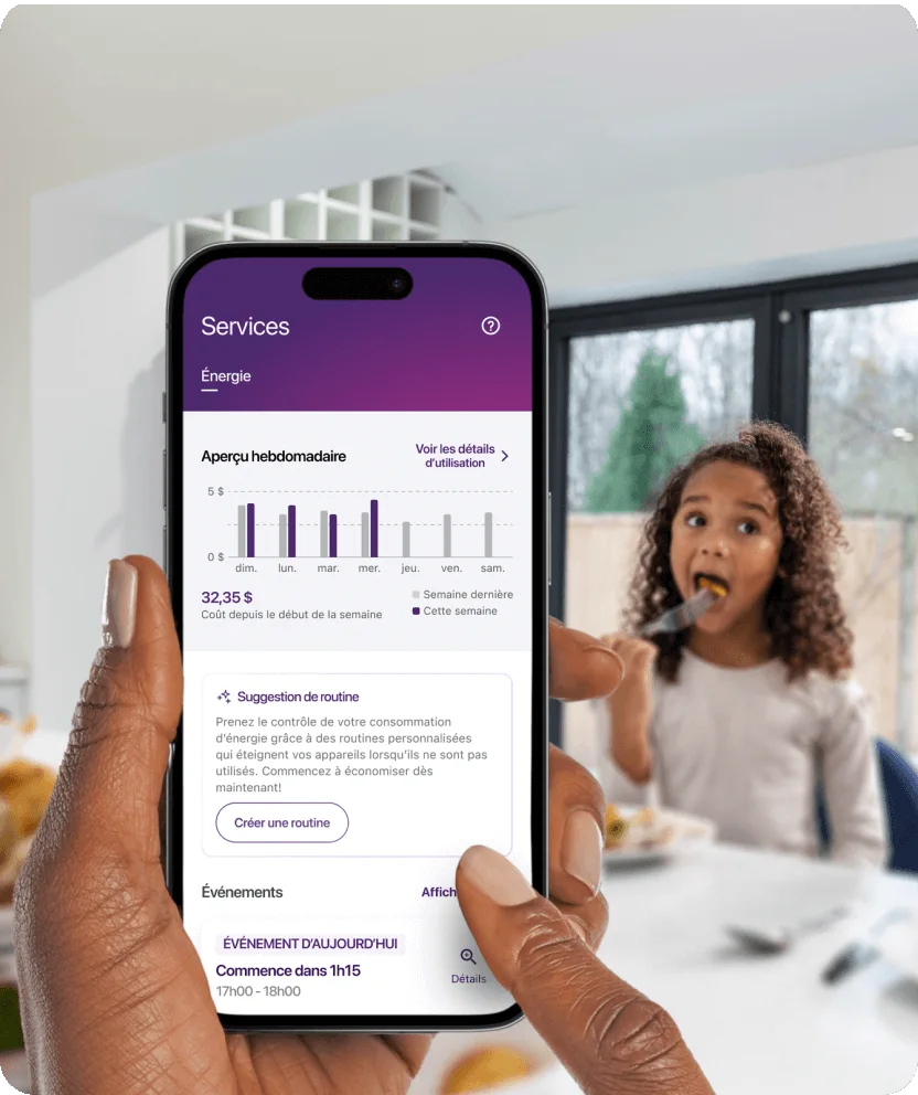 Une main tient un téléphone intelligent qui affiche les graphiques de consommation d’énergie, avec sa famille en arrière-plan