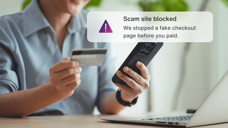 Woman holding a credit card and phone near a laptop, with a Scam site blocked alert popup.