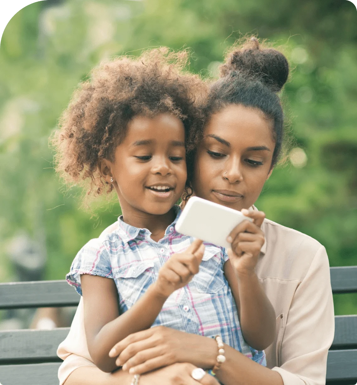 A parent and their child sitting on a bench while viewing a mobile device. 