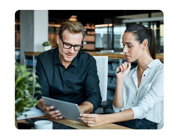 Homme et femme, assis sur un canapé, regardant un écran de tablette.