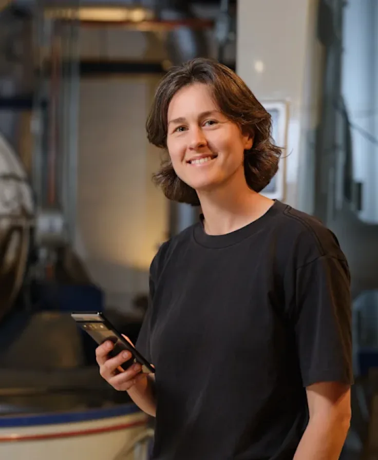 Owner of Dispatch Coffee holding a smartphone inside a coffee roasting facility.