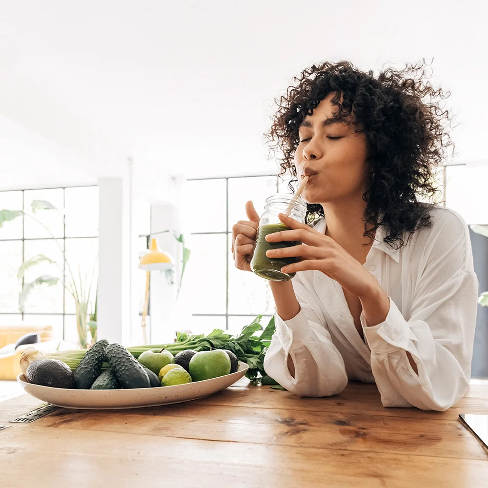 A woman sitting at a kitchen island drinking green juice