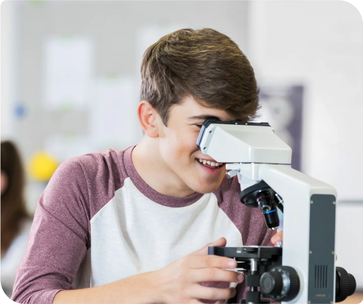 Un adolescent qui examine un objet à travers un microscope dans une classe.