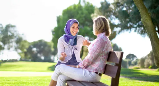 Deux femmes sont assises sur un banc de parc, sur une journée ensoleillé