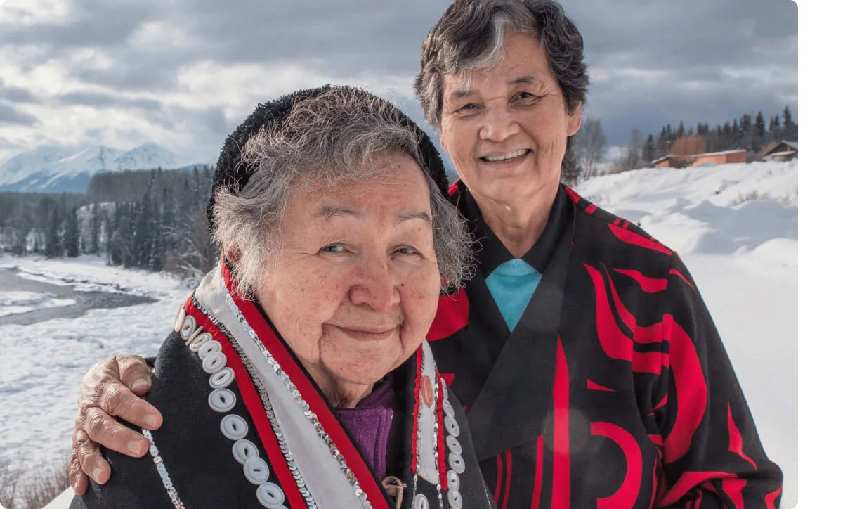 Two indigenous people in a snow-covered field smile.