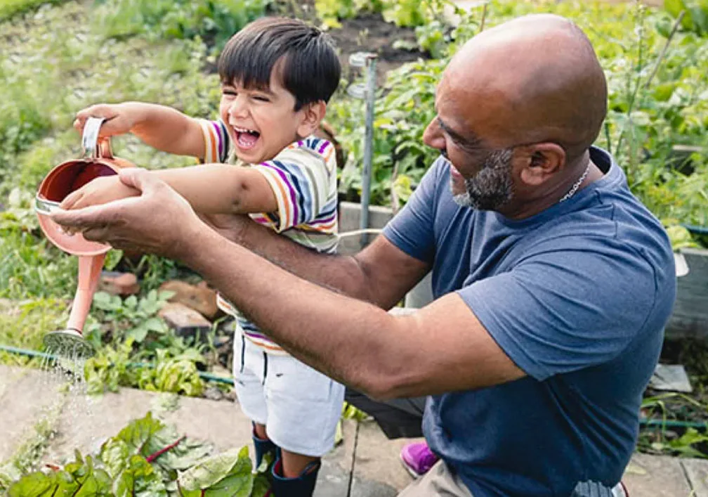 Man with young child smiling while watering the plants