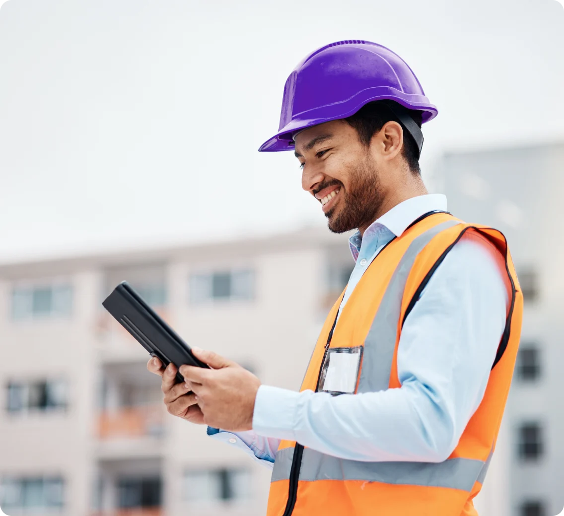 A man in a construction vest and hat looking at his tablet