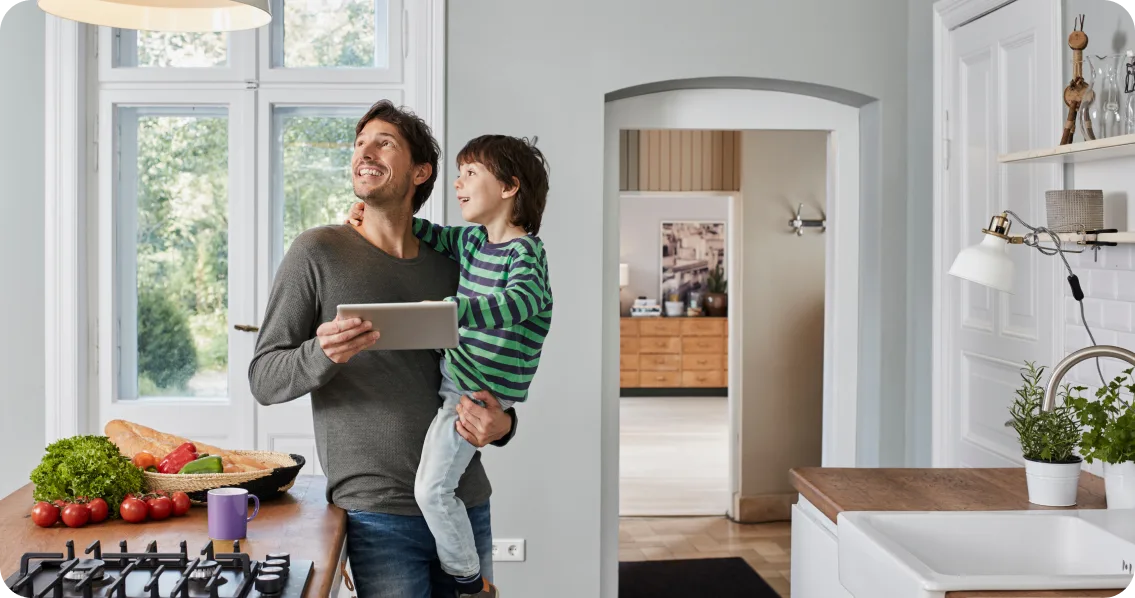 Un père tient un enfant dans une cuisine moderne avec des appareils Maison connectée