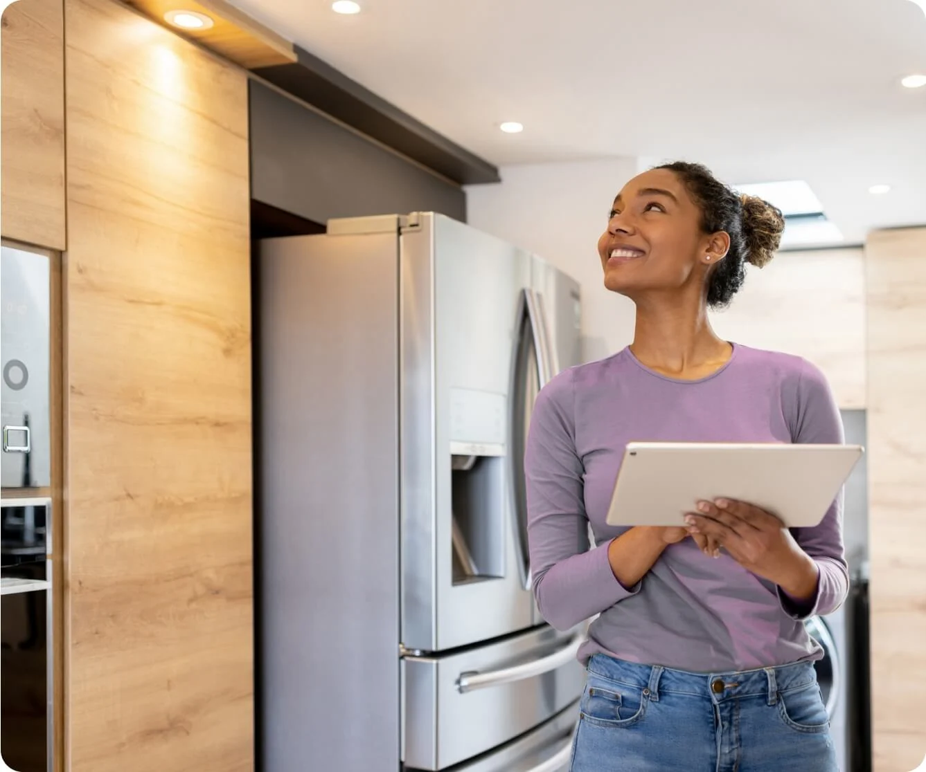Woman with tablet in modern kitchen looking up thoughtfully