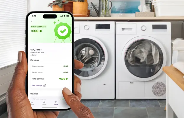 A hand holds the TELUS SmartHome+ app while doing the laundry and seeing a summary of a successful energy savings event completed. 