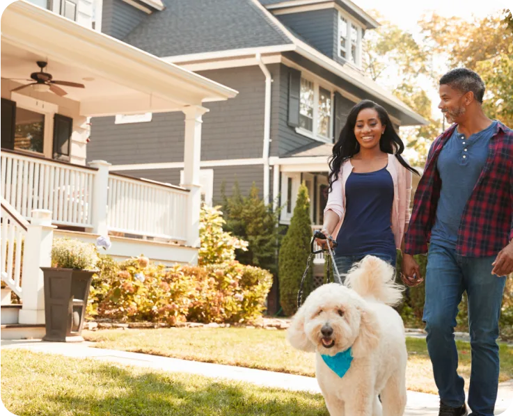 Couple se promenant avec un petit chien blanc devant leur maison