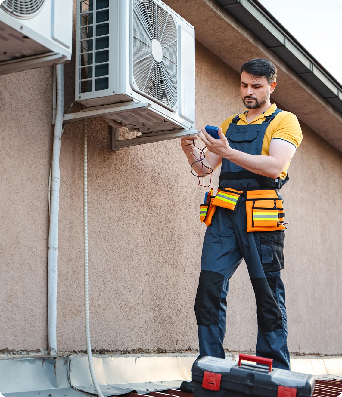 HVAC technician on a rooftop tests an outdoor AC unit with a meter.