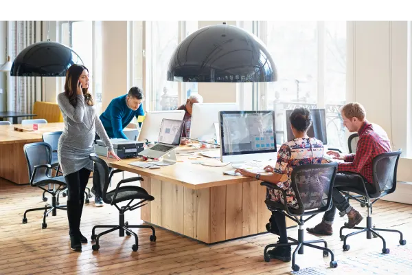 A group of five coworkers are sitting around a shared workstation, collaborating on a project.