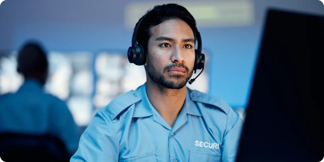 Un agent de sécurité portant un casque d’écoute surveille les alertes émises par un ordinateur de salle de contrôle.