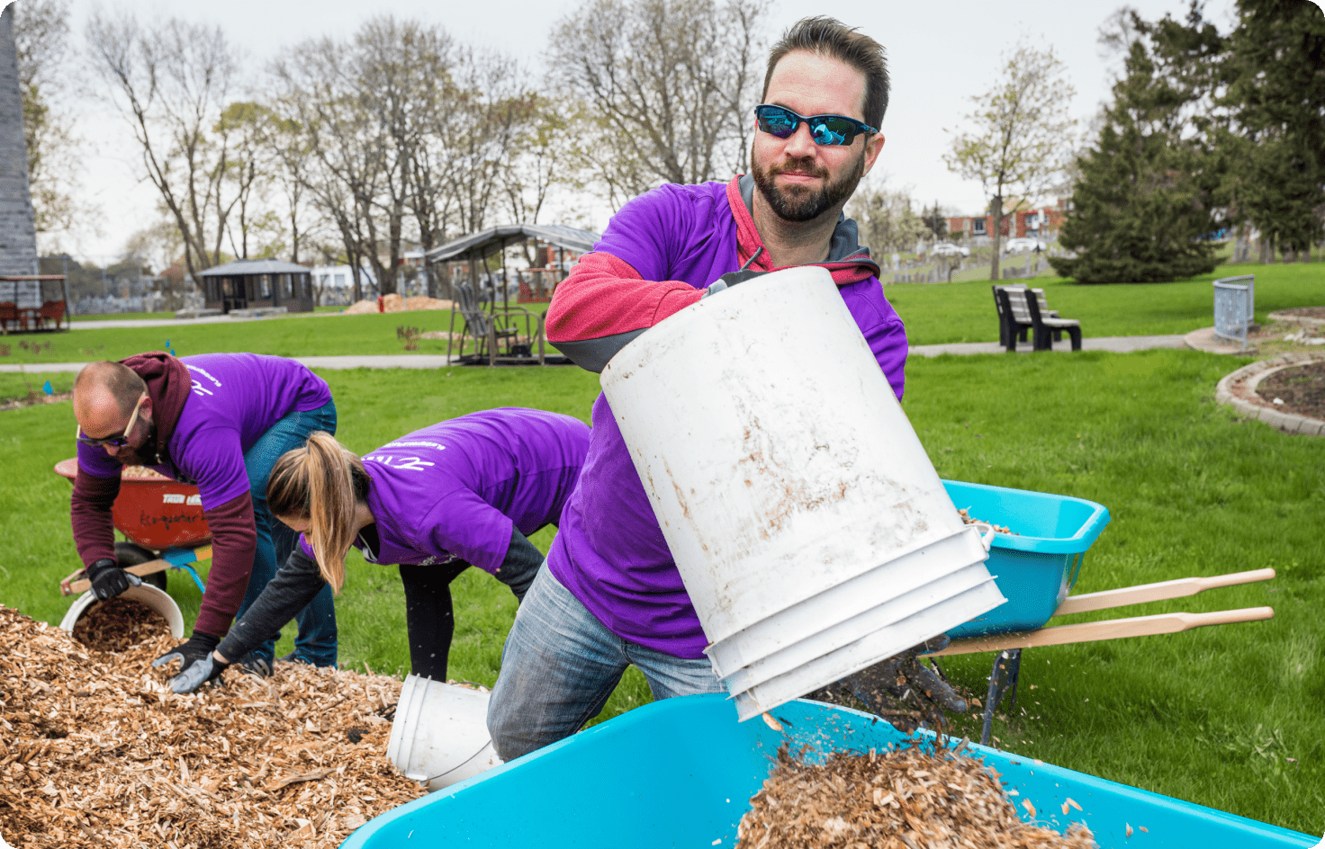 A TELUS team member emptying a bucket of woodchips into a wheelbarrow at the park.