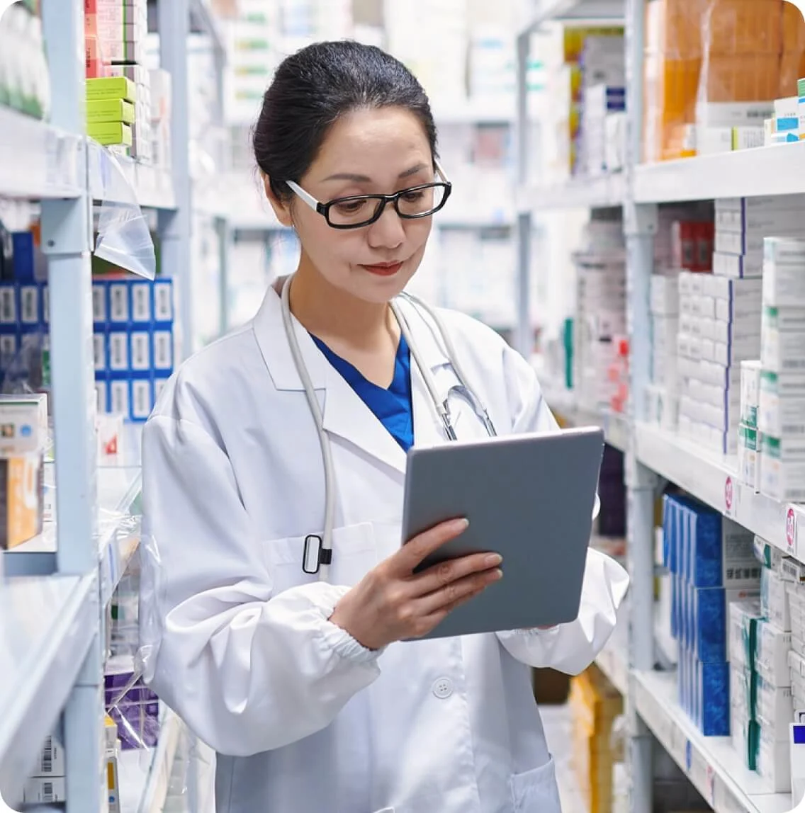 A female pharmacist in a pharmacy, focused on using a tablet to manage prescriptions and patient information.