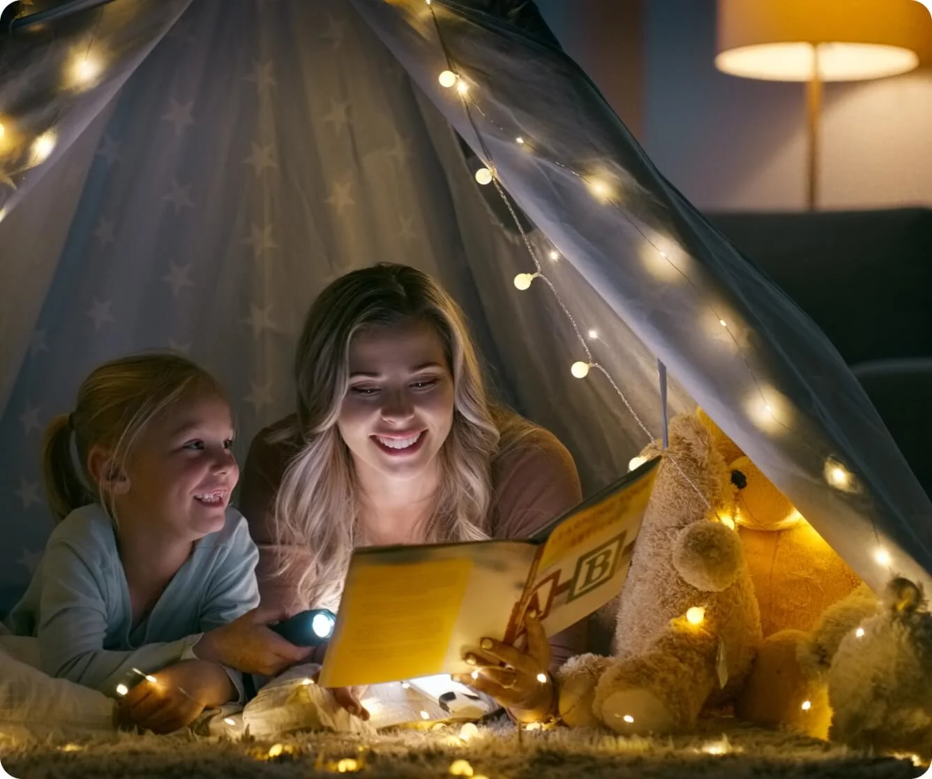 Children reading together under string lights in cozy tent
