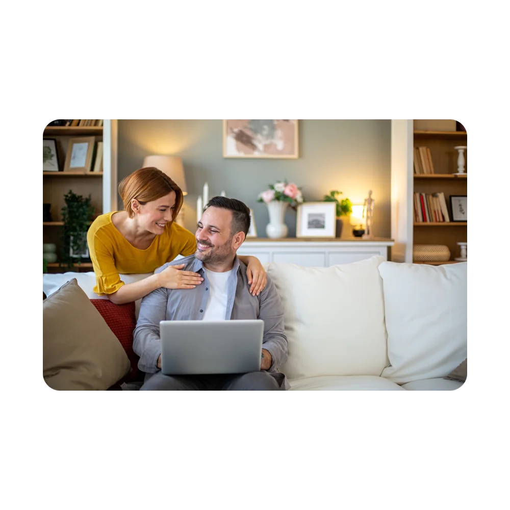 A couple sitting on a sofa and viewing their laptop.