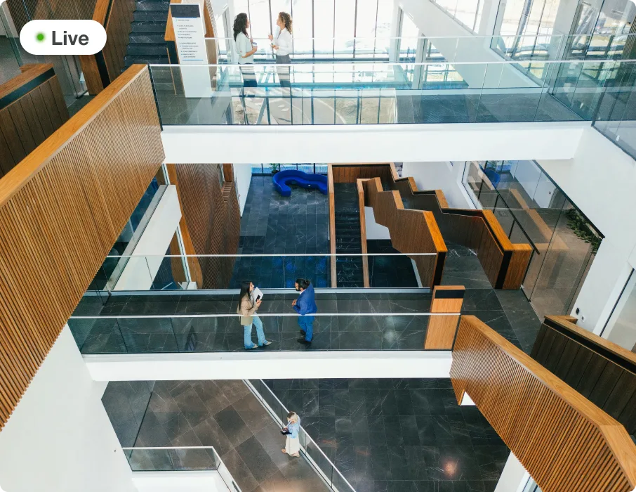 Live camera view of a modern office atrium with people talking on glass walkways.