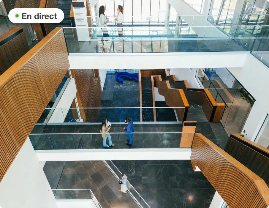 ue caméra en direct d’un atrium de bureaux moderne avec des gens qui discutent sur des passerelles vitrées.