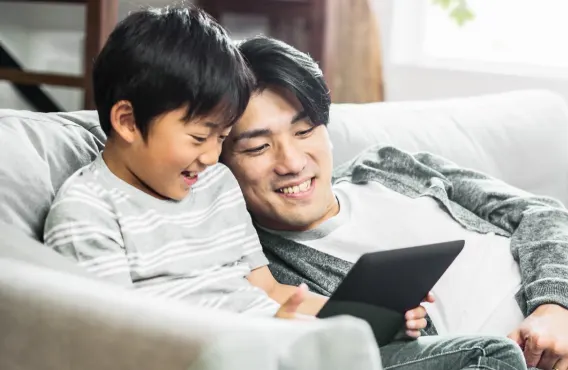 A father and son sit together on the couch watching a tablet, enjoying fast internet speeds from TELUS.